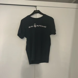 Svart t-shirt från Sail Racing - Snygg svart t-shirt från Sail Racing med tryckt logga på bröstet. Perfekt för en avslappnad stil. Kortärmad och tillverkad i ett mjukt material för extra komfort.