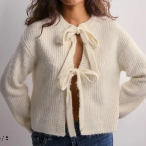 Vit stickad kofta med knytband - Säljer en mysig vit stickad kofta med knytband framtill. Koftan har en ribbad struktur och långa ärmar, perfekt för kyligare dagar. Köpte storlek M men jag torktumla den så den har blivit lite mindre skulle nog säga den är som storlek s nu! Aldrig använt.