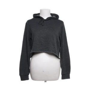 Mörkgrå croppad hoodie från Brandy Melville - Säljer en mörkgrå croppad hoodie från Brandy Melville. Den har en bekväm huva med dragsko och långa ärmar. Tillverkad i en mjuk blandning av bomull och polyester, perfekt för en avslappnad stil.