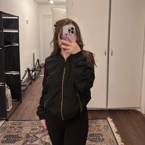 Svart bomberjacka - Snygg svart bomberjacka med dragkedja framtill och långa ärmar. Perfekt för en cool och avslappnad stil.