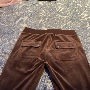 Bruna mjukisbyxor från Juicy Couture - Snygga bruna mjukisbyxor från Juicy Couture med snörning i midjan och praktiska bakfickor med knappar. Perfekta för en avslappnad stil.❤️