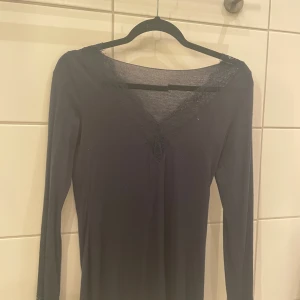 Mörkblå långärmad topp med spetsdetaljer - Elegant mörkblå långärmad topp med v-ringning och spetsdetaljer vid hals och ärmslut. Perfekt för en stilren look. Nypris 450kr