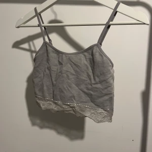 Grå linnetopp med spetsdetalj - Snygg grå linnetopp med smala axelband och spetsdetalj längs nederkanten. Perfekt för varma dagar eller som ett lager under en tröja.
