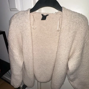 Beige stickad kofta från Lindex - Mysig beige stickad kofta från Lindex. Perfekt för kyliga dagar med sin mjuka och bekväma passform. Koftan har en öppen design utan knappar och långa ärmar.