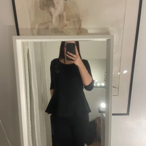 Svart topp med trekvartsärm - Snygg svart topp med trekvartsärm och en lätt utsvängd nederdel. Perfekt för en stilren look.