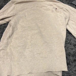 Beige tröja från Tommy Hilfiger - Säljer en stilren beige tröja från Tommy Hilfiger i en mjuk blandning av bomull och silke. Tröjan har en liten logotyp på bröstet och långa ärmar. Perfekt för en avslappnad och elegant look.