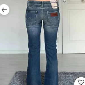 Blå bootcut jeans från Wrangler - Midjemåttet är 36cm och innebenslängden är 80cm Snygga blå bootcut jeans från Wrangler med klassisk femficksdesign och läderdetalj på bakfickan. Perfekta för en avslappnad stil med en touch av retro. De har en lågmidjad passform och är tillverkade i slitstarkt denim.