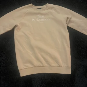 Beige sweatshirt från Peak Performance - Säljer en stilren beige sweatshirt från Peak Performance. Tröjan har en klassisk design med rund hals och långa ärmar. Perfekt för en avslappnad look. Peak Performance-loggan är tryckt på framsidan.