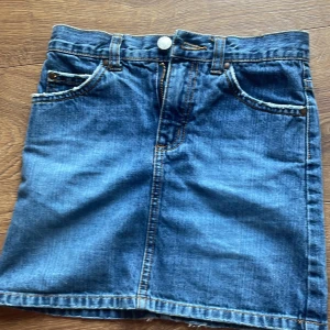 Blå jeanskjol - Snygg blå jeanskjol med klassisk femficksdesign och dragkedja fram. Perfekt för en avslappnad stil. Kjolen har bälteshällor och en knappstängning i midjan. Jag vet inte helt vad för storlek det är men jag tror att det är rätt. Dom är för små för mig så jag vill sälja dom❤️31 vid midjan.
