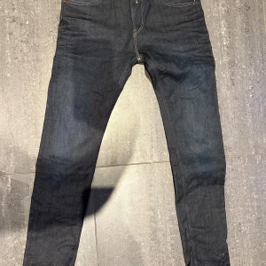 Mörkblå jeans från Replay - Snygga mörkblå jeans från Replay med klassisk femficksdesign och guldfärgade sömmar. Perfekta för en stilren look. Passformen är slim och de har en dragkedja i gylfen.
