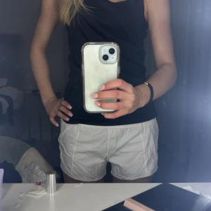 Vita shorts från Lululemon - Säljer ett par vita shorts från Lululemon. De är perfekta för träning med en bekväm passform och elastisk midja. Shortsen har en stilren design och är tillverkade i ett lätt och andningsbart material.