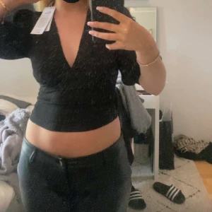 Svart topp från Gina tricot  - Säljer en stilren svart topp med puffärmar och v-ringning. Toppen har en tight passform och är perfekt för att ge en elegant touch till din outfit. Passar bra till både jeans och kjol.