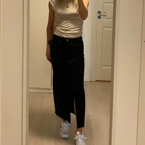 Svart långkjol från Stradivarius - Snygg svart långkjol från Stradivarius i jeansmaterial. Kjolen har en slits framtill och klassisk femficksdesign. Perfekt för en stilren look.