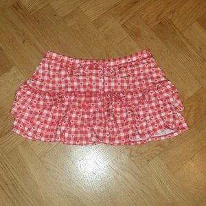 Rutig kjol med hjärtan från Urban Renewal - Charmig rutig kjol i rött och vitt med hjärtmönster från Urban Renewal. Kjolen har volanger som ger en lekfull look. Perfekt för att addera lite sötma till din outfit!