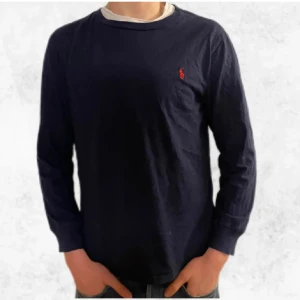 Mörkblå långärmad tröja från Ralph Lauren - Säljer en stilren mörkblå långärmad tröja från Ralph Lauren med det klassiska röda logotypen på bröstet. Perfekt för en avslappnad och snygg look. Tröjan är i storlek L och passar utmärkt till både jeans och chinos.