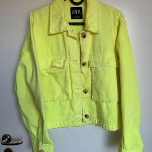 Gul jeansjacka från Zara - Säljer en cool gul jeansjacka från Zara med knappar framtill och två bröstfickor. Jackan har en klassisk krage och långa ärmar med knappdetaljer vid ärmsluten. Perfekt för att lysa upp din garderob! 💛Storlek M