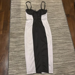 Svart och grå  klänning med axelband - Elegant svart och grå klänning med smala axelband och en figurnära passform. Klänningen har en stilren design med kontrasterande paneler och en hjärtformad urringning.