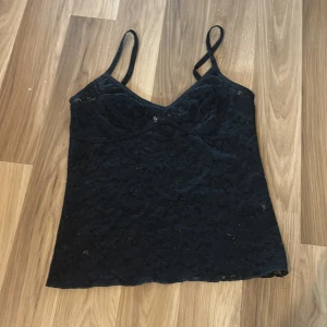 Svart spetslinne - Säljer ett svart spetslinne från kappahl med smala axelband och v-ringning. Perfekt för en elegant och stilren look. Linnet har ett vackert spetsmönster som ger en feminin touch.