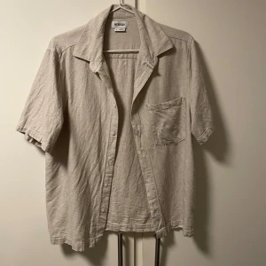 Beige linneskjorta från Weekday - Snygg beige kortärmad skjorta från Weekday i linne. Perfekt för varma dagar med en avslappnad passform och klassisk krage. Den är inte struken…men stryker den innan den levereras! Den passar bäst personer mellan 170-180cm!