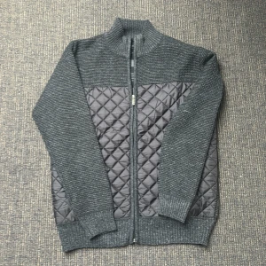 Grå quiltad cardigan  - Säljer en stilren grå kofta med quiltade detaljer och dragkedja framtill. Insidan har ett rutigt mönster i svart och vitt sjukt unikt. Perfekt för kyliga dagar! Aldrig använd, sjukt bra kvalite!