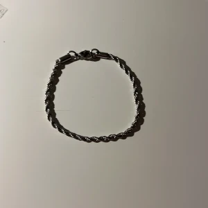Silverfärgat armband med tvinnad design -  Helt nytt Elegant silverfärgat armband med en tvinnad design. Perfekt för att ge en stilren touch till din outfit. Armbandet har en säker låsning och är lätt att bära.