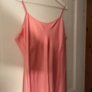 Rosa sidenklänning med tunna axelband - Elegant rosa klänning i siden med tunna axelband. Perfekt för en somrig look med sin mjuka och glansiga finish. Klänningen har en enkel och stilren design som ger en lyxig känsla.