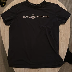 Svart t-shirt från Sail Racing - Snygg svart t-shirt från Sail Racing med tryck på bröstet och en liten logga på baksidan. Perfekt för en avslappnad stil.