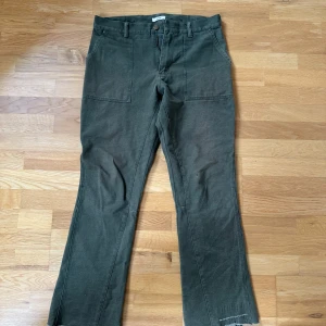 Gröna byxor från O Files - Snygga gröna byxor från O Files med en avslappnad passform. Byxorna har framträdande fickor och en rå kant vid bensluten för en cool look. Perfekta för en casual stil.