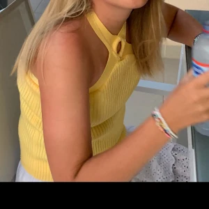 Gul ribbad halterneck topp - Säljer en solgul ribbad halterneck topp med knytning i nacken. Perfekt för varma sommardagar. Toppen har en stilren design med korsade band på baksidan.