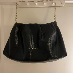 Svart axelväska från Valentino by Mario  - Används ganska flitigt men utan skada på väskan. Märke: Valentino by Mario Valentino. Mått: Bredd: ca 38-40 cm, Höjd: ca 19-21 cm 