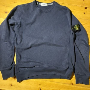 Mörkblå tröja från Stone Island - Säljer en snygg mörkblå tröja från Stone Island med deras ikoniska märke på ärmen. Tröjan har en rund halsringning och långa ärmar. Perfekt för en stilren look. Hör av dig vid frågor🙏(XL men passar L,M då Stone Island är små i storlek)
