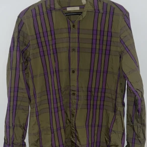 Grön och lila randig skjorta från Burberry - Säljer en stilren grön och lila randig skjorta från Burberry. Skjortan har långa ärmar och knappar framtill. Perfekt för dig som vill ha en unik och färgglad stil. Passar (M&L)