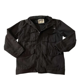 Svart Dcate Jacka - Säljer en stilren svart jacka från Dcate med lite workwear känsla. Jackan har även en luva som sitter inuti kragen. Perfekt för höst och vår. Storlek XS men passar som en S-M