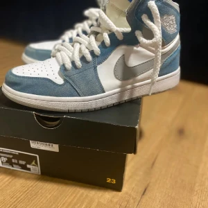 Air Jordan 1 Mid - Vit/Blå Suede (Storlek 42, EUR) - Säljer mina Air Jordan 1 Mid i den snygga färgkombinationen vit och blå suede. Skorna är i bra skick och har knappt använts, så de ser fortfarande ut som nya. Detta är ett populärt och eftertraktat par, perfekt för både vardagsbruk och för sneaker-sa