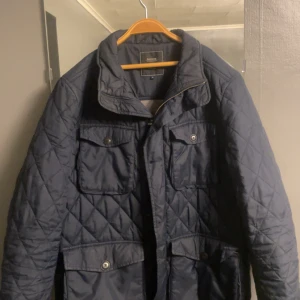 Mörkblå Field Jacket från Boomerang - Säljer en snygg mörkblå quiltad jacka från Boomerang i storlek M. Jackan har en klassisk design med dragkedja och knappar framtill, samt praktiska fickor. Perfekt för höst och vår när du vill hålla stilen och värmen. 🧥
