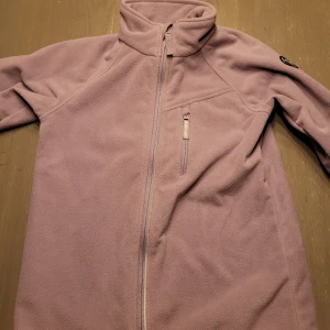 Lila fleecejacka från Polarn O. Pyret - Mysig lila fleecejacka från Polarn O. Pyret i storlek 140. Perfekt för kyliga dagar med dragkedja framtill och en liten bröstficka. Jackan har en hög krage för extra värme och är i mycket bra skick. Perfekt för höst och vår!