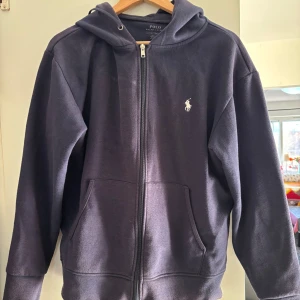 Mörkblå zip hoodie från Polo Ralph Lauren - Säljer en stilren mörkblå hoodie från Polo Ralph Lauren i bra skick. Den har en dragkedja framtill och en klassisk logga på bröstet. Perfekt för både höst och vår, och passar till alla tillfällen. Superbekväm och snygg! Skriv i Dm ifall ni vill diskutera pris!