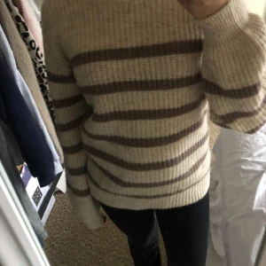 Randig stickad tröja från Pieces - Mysig stickad tröja från Pieces i beige och bruna ränder. Perfekt för höst och vinter med sin varma och bekväma passform. Tröjan har långa ärmar och en klassisk rund halsringning. Perfekt för en avslappnad stil eller att mysa i hemma. 🧶