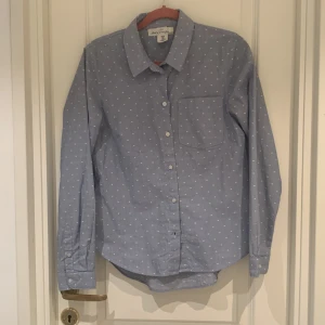 Blå prickig skjorta från Land's End - Säljer en snygg blå skjorta från Land's End i storlek M. Skjortan har ett diskret prickigt mönster och en bröstficka. Perfekt för både vardag och fest! Den är i mycket bra skick och har långa ärmar med knappar framtill.