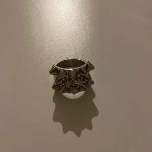 Cool och edgy silvrig ring med nitar runtom. Perfekt för att ge din outfit en tuff touch. Ringen har en bred design och är i metalliskt silver. Passar både till vardags och festliga tillfällen.