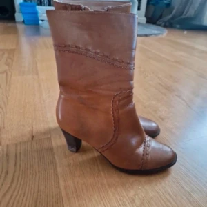 Bruna skinnstövletter med klack - Säljer ett par snygga bruna stövletter i skinn med klack. De har dekorativa sömmar och dragkedja på sidan för enkel på- och avtagning. Perfekta för höst och vår, och ger en stilren touch till vilken outfit som helst.