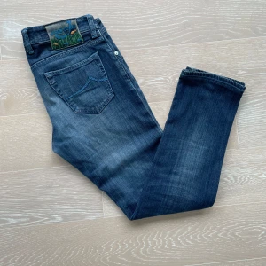 Blå jeans från Jacob Cohen - Säljer ett par snygga blå jeans från Jacob Cohen. De är i bra skick och har en klassisk taperd fit Jeansen har en cool broderad detalj på bakfickan och är tillverkade av högkvalitativt denim. Perfekta för både vardag och fest!