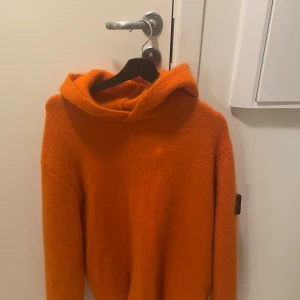 Orange hoodie Stone Island - Säljer en snygg orange hoodie från Stone Island i mycket bra skick. Den är perfekt för höst och vinter med sin varma och mjuka känsla. Hoodien har en klassisk design med en stor huva och det ikoniska Stone Island-märket på ärmen. Perfekt för att hålla stilen när det blir kallt ute! 🍂Gjord i filtliknande material.