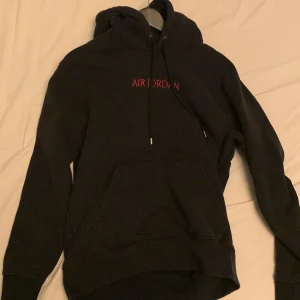 Svart hoodie från Air Jordan - Säljer en snygg svart hoodie från Air Jordan i bra skick. Den har en broderad logga i rött på bröstet och en klassisk känguruficka framtill. Perfekt för höst och vinter, och passar både till vardags och träning. Huvan har dragsko för justerbar passform.