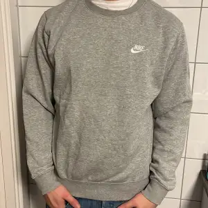 Säljer en klassisk grå sweatshirt från Nike i mycket bra skick. Den har en normal passform med långa ärmar och en rund halsringning. Perfekt för både vardag och träning. Nike-loggan är broderad i vitt på bröstet. Superbekväm och stilren! Skick 9/10 inga fel överhuvudtaget.