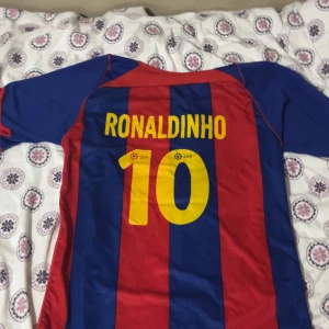 barcelona ronaldinho tröja  - Säljer en klassisk  Barcelona fotbollströja med Ronaldinho och nummer 10 på ryggen. Tröjan är i de ikoniska blå och röda färgerna med klubbmärket på framsidan. Perfekt för fans av den legendariska spelaren! 🏆(ingen aning om den är äkta eller inte)