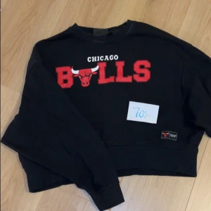 Svart Chicago Bulls sweatshirt - Säljer en cool svart Chicago Bulls sweatshirt med röd logga och text. Tröjan är croppad och har långa ärmar, perfekt för en avslappnad stil. Passar bra till både jeans och leggings. Perfekt för höst och vår!