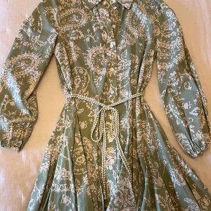 Grön mönstrad klänning med knytband från Zara - Säljer en superfin grön klänning med vitt mönster och knytband i midjan. Klänningen har långa ärmar och en klassisk krage. Perfekt för vår och sommar! 🌿