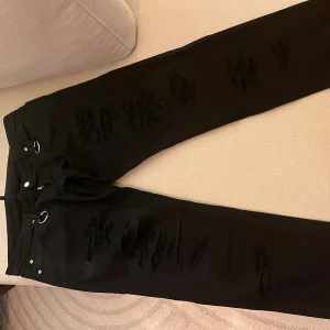 Svarta jeans från Dsquared2 - Säljer ett par svarta jeans från Dsquared2 i bra skick. De har en cool distressed look med slitningar och silverfärgade ringdetaljer vid midjan. Perfekta för en edgy stil! 🖤