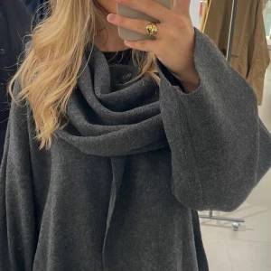 Mörkgrå kappa med halsduk  - Säljer en superfin mörkgrå kappa med en stor, mysig halsduk som ger en cool look. Perfekt för höst och vinter! Den har långa ärmar och en lös passform som gör den bekväm att bära över tjockare tröjor. Passar både till vardags och fest. 🖤knappt använd 🫶🏼